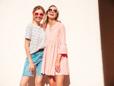 Son moda yaz kıyafetleri ve elbiseleri içinde gülümseyen iki güzel hippi kadın. Sokakta poz veren kaygısız kadınlar. Pozitif saf modeller gün batımında eğleniyorlar, sarılıyorlar ve deliriyorlar.