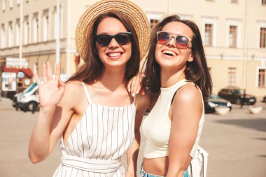 Son moda yaz kıyafetleri içinde iki güzel gülümseyen yeniyetme kadın. Sokakta şapkalı kayla poz veren kaygısız kadınlar. Pozitif saf modeller gün batımında eğleniyorlar.