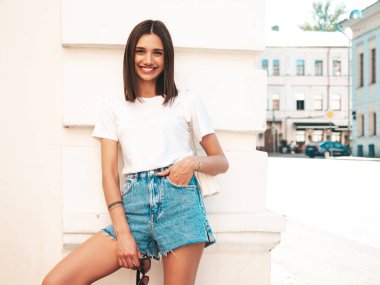 Güzel gülümseyen hippi bir kadının son moda kot şortlu portresi. Günbatımında sokakta poz veren kaygısız seksi manken. Güneş gözlüklü, açık hava modeli.