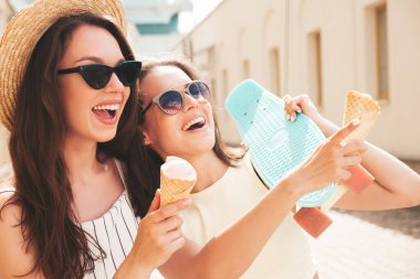 Son moda yaz kıyafetleri ve elbiseleri içinde gülümseyen iki güzel hippi kadın. Sokakta poz veren kaygısız kadınlar. Pozitif modeller gün batımında waffle külahında lezzetli dondurmalar yiyorlar.