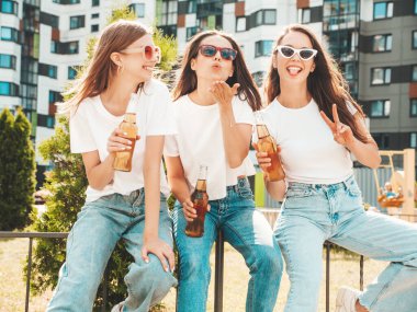 Üç güzel, güler yüzlü yeniyetme kadın aynı yaz kıyafetleri içinde. Sokakta poz veren kaygısız kadınlar. Güneş gözlükleriyle eğlenen pozitif modeller. Şişe bira içmek. Ekim Festivali