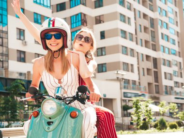 Son moda giyinmiş iki güzel, gülümseyen yeniyetme kadın. Sokakta geçmişe dönük motosiklet süren kaygısız kadınlar. Eğlenceli ve klasik İtalyan mobiletleriyle gezen pozitif modeller.