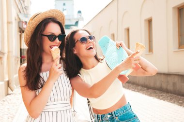 Son moda yaz kıyafetleri ve elbiseleri içinde gülümseyen iki güzel hippi kadın. Sokakta poz veren kaygısız kadınlar. Pozitif modeller gün batımında waffle külahında lezzetli dondurmalar yiyorlar.