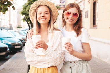 Son moda yaz kıyafetleri içinde iki güzel gülümseyen hippi kadın. Sokakta poz veren kaygısız kadınlar. Pozitif saf modeller gün batımında eğleniyorlar. Kahve ya da çay içiyorlar.