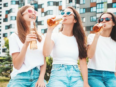 Üç güzel, güler yüzlü yeniyetme kadın aynı yaz kıyafetleri içinde. Sokakta poz veren kaygısız kadınlar. Güneş gözlükleriyle eğlenen pozitif modeller. Şişe bira içmek. Ekim Festivali