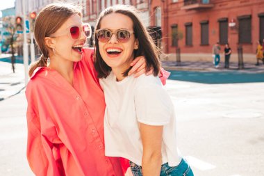 Son moda beyaz tişörtlü ve kot pantolonlu iki güzel, gülümseyen yeniyetme bayan sokak arka planında poz veren kaygısız kadınlar. Pozitif modeller eğleniyor, sarılıyor ve deliriyor.
