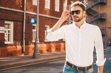 Yakışıklı, kendine güvenen, stil sahibi, Lambersex mankeni portresi. Beyaz gömlek giymiş modern bir adam. Sokakta poz veren düşünceli bir erkek. Gün batımında güneş gözlükleriyle dışarıda.