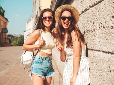 Son moda yaz kıyafetleri içinde iki güzel gülümseyen yeniyetme kadın. Sokakta şapkalı kayla poz veren kaygısız kadınlar. Pozitif saf modeller gün batımında eğleniyorlar.