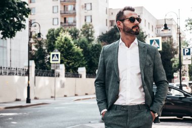 Yakışıklı, kendine güvenen, stil sahibi, lamberseksüel bir modelin portresi. Zarif takım elbise giymiş modern bir adam. Moda erkeği gün batımında Avrupa şehrinin arka planında poz veriyor. Güneş gözlükleriyle