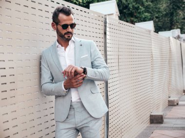 Yakışıklı, kendine güvenen, stil sahibi, lamberseksüel bir modelin portresi. Zarif beyaz takım elbise giymiş modern bir adam. Moda erkeği gün batımında Avrupa şehrinin arka planında poz veriyor. Güneş gözlükleriyle