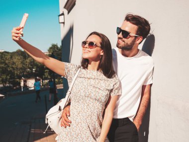 Gülümseyen güzel kadın ve yakışıklı erkek arkadaşı. Gündelik yaz kıyafetleri giymiş bir kadın. Mutlu, neşeli bir aile. Kadın eğleniyor. Duvarın yanında poz veren bir çift. Birbirlerine sarılıyorlar. Selfie çekiyorum.