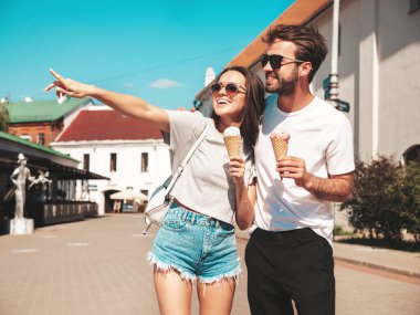 Gülümseyen güzel kadın ve yakışıklı erkek arkadaşı. Gündelik yaz kıyafetleri giymiş bir kadın. Mutlu, neşeli bir aile. Sokakta güneş gözlüklü bir çift poz veriyor. Waffle külahında lezzetli dondurma yemek.