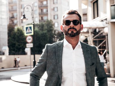 Yakışıklı, kendine güvenen, stil sahibi, lamberseksüel bir modelin portresi. Zarif takım elbise giymiş modern bir adam. Moda erkeği gün batımında Avrupa şehrinin arka planında poz veriyor. Güneş gözlükleriyle