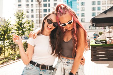 Son moda yaz kıyafetleri içinde iki güzel, gülümseyen hippi kadın. Pembe saçlı, sokakta poz veren kaygısız kadınlar. Pozitif saf modeller gün batımında eğleniyorlar. Neşeli ve mutlu