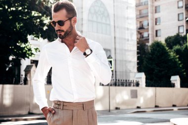 Yakışıklı, kendine güvenen, stil sahibi bir hipster Lambersexual modelin portresi. Beyaz gömlek ve pantolon giymiş modern bir adam. Moda erkeği gün batımında Avrupa şehrinin arka planında poz veriyor. Güneş gözlükleriyle