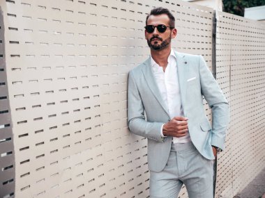 Yakışıklı, kendine güvenen, stil sahibi, lamberseksüel bir modelin portresi. Zarif beyaz takım elbise giymiş modern bir adam. Moda erkeği gün batımında çitlerin yanında poz veriyor. Güneş gözlükleriyle