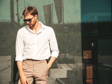 Yakışıklı, kendine güvenen, stil sahibi, Lambersex mankeni portresi. Beyaz gömlek giymiş modern bir adam. Moda erkeği güneş gözlükleriyle sokakta poz veriyor.