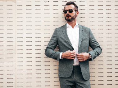 Yakışıklı, kendine güvenen, stil sahibi, lamberseksüel bir modelin portresi. Zarif takım elbise giymiş modern bir adam. Moda erkeği gün batımında çitin yanında poz veriyor. Güneş gözlükleriyle