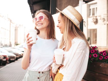 Son moda yaz kıyafetleri içinde iki güzel gülümseyen hippi kadın. Sokakta poz veren kaygısız kadınlar. Pozitif saf modeller gün batımında eğleniyorlar. Kahve ya da çay içiyorlar.