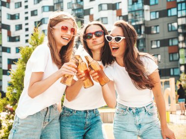 Üç güzel, güler yüzlü yeniyetme kadın aynı yaz kıyafetleri içinde. Sokakta poz veren kaygısız kadınlar. Güneş gözlükleriyle eğlenen pozitif modeller. Şişe bira içmek. Ekim Festivali