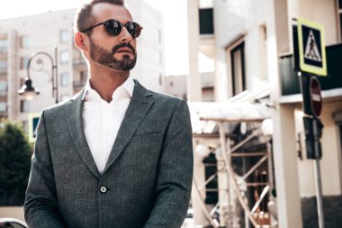 Yakışıklı, kendine güvenen, stil sahibi, lamberseksüel bir modelin portresi. Zarif takım elbise giymiş modern bir adam. Moda erkeği gün batımında Avrupa şehrinin arka planında poz veriyor. Güneş gözlükleriyle