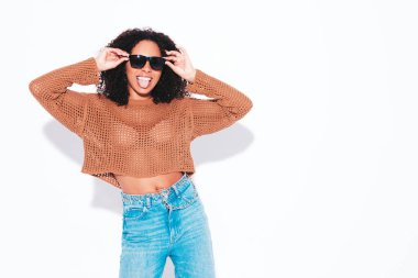 Saçları kıvırcık, güzel siyah bir kadın. Moda kıyafetleri içinde gülümseyen bir model. Stüdyonun beyaz duvarında güneş gözlükleriyle izole edilmiş seksi, kaygısız kadın. Bronzlaşmış ve neşeli. Dili nasıl? 