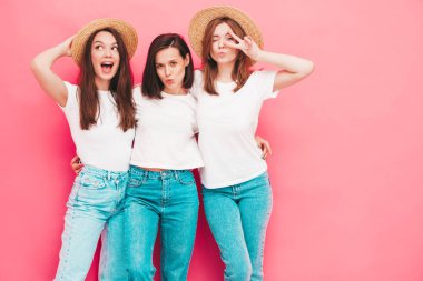 Aynı yaz moda olan beyaz tişört ve kot pantolon giyen üç güzel, gülümseyen hippi kadın. Stüdyoda pembe duvarın yanında poz veren kaygısız seksi kadınlar. Şapkalı pozitifler