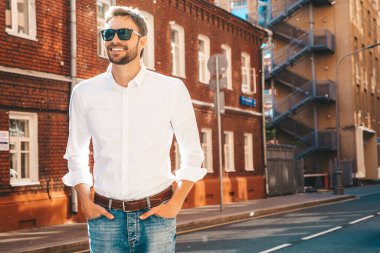 Yakışıklı, kendine güvenen, stil sahibi, Lambersex mankeni portresi. Beyaz gömlek giymiş modern bir adam. Moda erkeği, güneş gözlüklü gökdelenlerin yanında sokak arkasında poz veriyor.