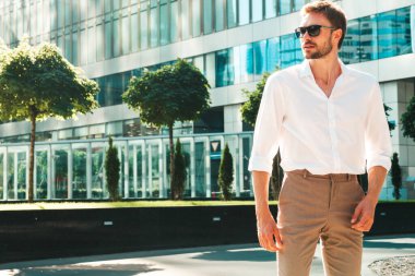 Yakışıklı, kendine güvenen, stil sahibi, Lambersex mankeni portresi. Beyaz gömlek giymiş modern bir adam. Moda erkeği, güneş gözlüklü gökdelenlerin yanında sokak arkasında poz veriyor.