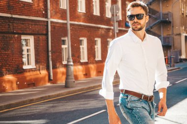 Yakışıklı, kendine güvenen, stil sahibi, Lambersex mankeni portresi. Beyaz gömlek giymiş modern bir adam. Sokakta poz veren düşünceli bir erkek. Gün batımında güneş gözlükleriyle dışarıda.