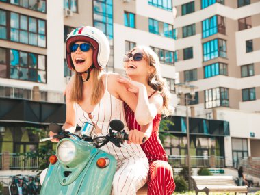 Son moda giyinmiş iki güzel, gülümseyen yeniyetme kadın. Sokakta geçmişe dönük motosiklet süren kaygısız kadınlar. Eğlenceli ve klasik İtalyan mobiletleriyle gezen pozitif modeller.