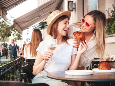 Son moda yaz kıyafetleri içinde iki güzel gülümseyen yeniyetme kadın. Sokakta Veranda Kafe 'de poz veren kaygısız kadınlar. Beyaz şarap içen pozitifler.