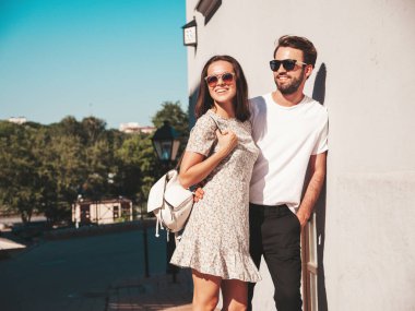 Gülümseyen güzel kadın ve yakışıklı erkek arkadaşı. Gündelik yaz kıyafetleri giymiş bir kadın. Mutlu, neşeli bir aile. Kadın eğleniyor. Arka planda poz veren bir çift. Gün batımında birbirlerine sarılıyorlar.