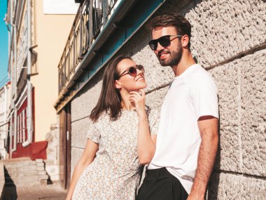 Gülümseyen güzel kadın ve yakışıklı erkek arkadaşı. Gündelik yaz kıyafetleri giymiş bir kadın. Mutlu, neşeli bir aile. Kadın eğleniyor. Arka planda poz veren bir çift. Gün batımında birbirlerine sarılıyorlar.