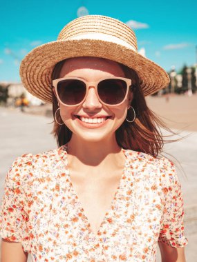 Moda kıyafetleri içinde gülümseyen genç ve güzel bir hippi kadın. Gün batımında plaj şapkasıyla sokakta poz veren kaygısız seksi kadın. Açık havada pozitif model. Neşeli ve mutlu güneş gözlükleriyle