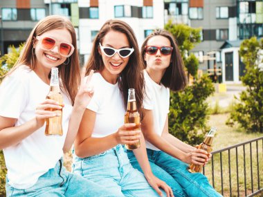 Üç güzel, güler yüzlü yeniyetme kadın aynı yaz kıyafetleri içinde. Sokakta poz veren kaygısız kadınlar. Güneş gözlükleriyle eğlenen pozitif modeller. Şişe bira içmek. Ekim Festivali