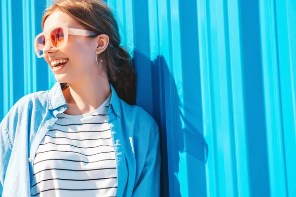 流行の夏服の若い美しい笑顔ヒップスター女性 日没時に青い壁の近くの通りの背景にポーズを取るセクシーな屈託のない女性 肯定的なモデルは屋外 陽気で幸せなサングラス — ストック写真