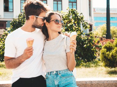 Gülümseyen güzel kadın ve yakışıklı erkek arkadaşı. Gündelik yaz kıyafetleri giymiş bir kadın. Mutlu, neşeli bir aile. Sokakta güneş gözlüklü bir çift poz veriyor. Waffle külahında lezzetli dondurma yemek.