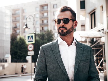 Yakışıklı, kendine güvenen, stil sahibi, lamberseksüel bir modelin portresi. Zarif takım elbise giymiş modern bir adam. Moda erkeği gün batımında Avrupa şehrinin arka planında poz veriyor. Güneş gözlükleriyle