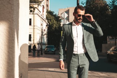 Yakışıklı, kendine güvenen, stil sahibi, lamberseksüel bir modelin portresi. Zarif takım elbise giymiş modern bir adam. Moda erkeği gün batımında Avrupa şehrinin arka planında poz veriyor. Güneş gözlükleriyle