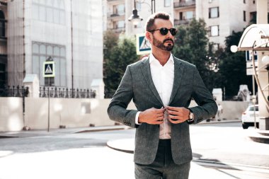 Yakışıklı, kendine güvenen, stil sahibi, lamberseksüel bir modelin portresi. Zarif takım elbise giymiş modern bir adam. Moda erkeği gün batımında Avrupa şehrinin arka planında poz veriyor. Güneş gözlükleriyle
