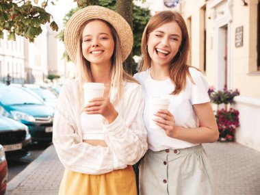 Son moda yaz kıyafetleri içinde iki güzel gülümseyen hippi kadın. Sokakta poz veren kaygısız kadınlar. Pozitif saf modeller gün batımında eğleniyorlar. Kahve ya da çay içiyorlar.