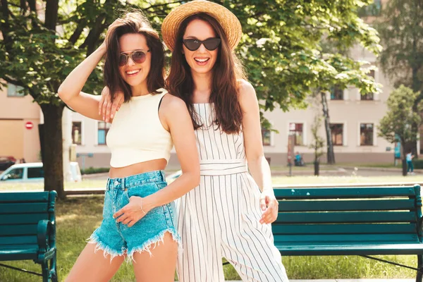 流行の夏服の2人の若い美しい笑顔ヒップスター女性 帽子の通りの背景にポーズ性的屈託のない女性 正の純粋なモデルは 日没で楽しみを持っています — ストック写真