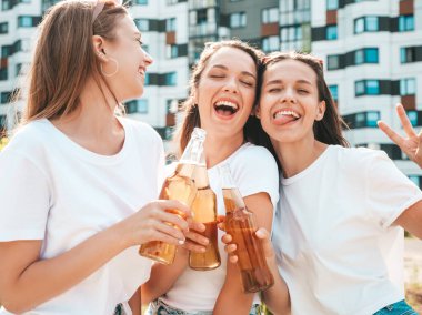 Üç güzel, güler yüzlü yeniyetme kadın aynı yaz kıyafetleri içinde. Sokakta poz veren kaygısız kadınlar. Güneş gözlükleriyle eğlenen pozitif modeller. Şişe bira içmek. Ekim Festivali