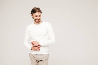 Beyaz süveter ve pantolon giyen yakışıklı, gülümseyen hippi, keresteci iş adamı modeli portresi. Stüdyoda gri arka planda poz veren modacı.