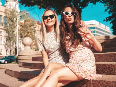 Son moda yaz kıyafetleri içinde iki güzel gülümseyen hippi kadın. Sokakta poz veren kaygısız kadınlar. Pozitif saf modeller gün batımında eğleniyor, sarılıyor ve deliriyor. Mutlu ve neşeli.