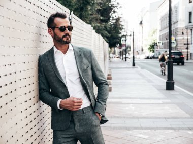 Yakışıklı, kendine güvenen, stil sahibi, lamberseksüel bir modelin portresi. Zarif takım elbise giymiş modern bir adam. Moda erkeği gün batımında Avrupa şehrinin arka planında poz veriyor. Güneş gözlükleriyle