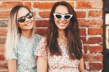 Son moda yaz kıyafetleri içinde iki güzel gülümseyen hippi kadın. Sokakta poz veren kaygısız kadınlar. Pozitif saf modeller gün batımında eğleniyor, sarılıyor ve deliriyor. Mutlu ve neşeli.