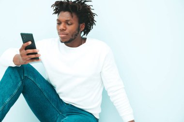 Yakışıklı, gülümseyen hipster modeli. Yazlık giysiler içinde traşsız Afrikalı bir adam. Stüdyoda mavi duvarda poz veren rastalı bir erkek. 