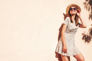 Moda kıyafetleri içinde gülümseyen genç ve güzel bir hippi kadın. Gün batımında plaj şapkalı, duvarın yanında poz veren kaygısız seksi kadın. Açık havada pozitif model. Neşeli ve mutlu güneş gözlükleriyle